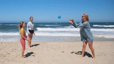 Anne ve iki çocuk sahilde birlikte oynuyorlar, aralarına su dolu bir balon atıyorlar. Neşeli oyun, parlak, güneşli bir gökyüzünün altında okyanus dalgaları tarafından gözler önüne seriliyor.