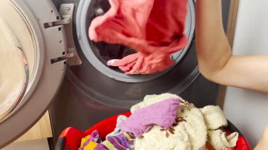 Bir kadın çamaşır makinesinden yeni yıkanmış ve örülmüş giysileri alır, çamaşır sepetine koyar, ev işlerini ve günlük temizlik rutinini tamamlar.