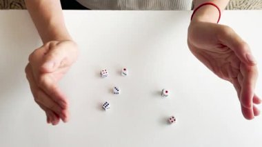 Beyaz bir masada zar oynayan bir kadının videosunu kapat. Sayılar, şans, kumar, masa oyunu unsurları, şans ve eğlence kavramlarıyla yuvarlanan küpler.