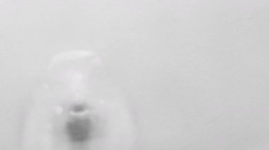 Close-up of a subtle water distortion pushing up a soft surface. Monochromatic light gray background with gentle lighting. Abstract tension forms an organic shape through transparent movement