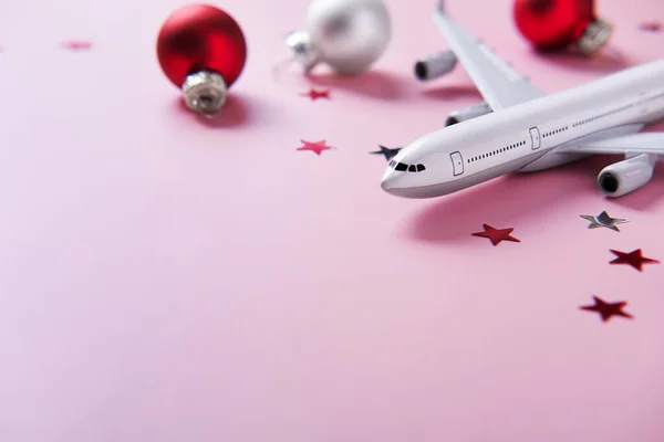 Christmas travel planning. Traveling as gift. White blank model of passenger plane and Christmas decorations on pink background. T Copy Space.