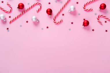 Noel kompozisyonu. Çubuk şekerlerden yapılmış sınırlar, pembe arka planda tatil süslemeleri. Noel, kış, yeni yıl konsepti. Düz konum, üst görünüm, kopyalama alanı