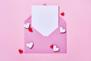 Sevgililer Günü veya Anneler Günü için tebrik kartı maketi. Zarfın içinde beyaz boş bir kart ve pembe arka planda dekoratif tahta kalpler..