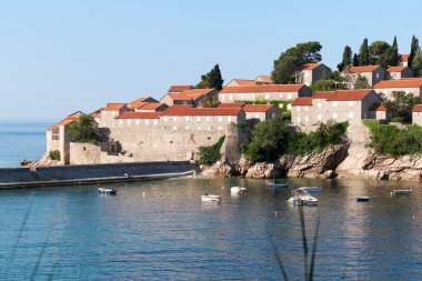 Karadağ 'ın Sveti Stefan adası yakınlarındaki sakin mavi deniz ve demirli tekneler. Adriyatik Denizi 'nde temiz deniz suyu olan bir adada butik oteli olan lüks turizm beldesi, Karadağ, 4K.