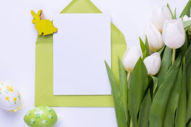Template for Easter greeting card. Blank card with an envelope, a bouquet of white tulips and decorative eggs and a rabbit.