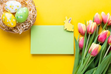 Template for Easter greeting card. Blank card with a bouquet of tulips and decorative eggs and a rabbit. Flat lay. Spring composition.