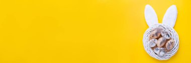 Easter banner with decorative white wreath, quail eggs and rabbit ears on yellow background