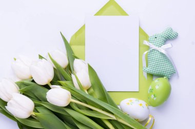 Template for Easter greeting card. Blank card with an envelope, a bouquet of white tulips and decorative eggs and a rabbit.