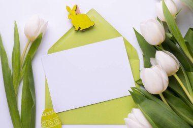 Template for Easter greeting card. Blank card with an envelope, a bouquet of white tulips and decorative eggs and a rabbit.