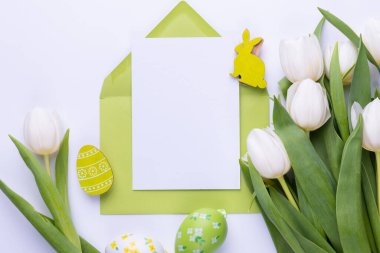 Template for Easter greeting card. Blank card with an envelope, a bouquet of white tulips and decorative eggs and a rabbit.