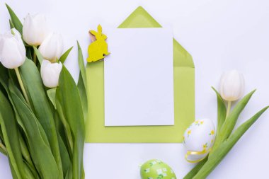 Template for Easter greeting card. Blank card with an envelope, a bouquet of white tulips and decorative eggs and a rabbit.