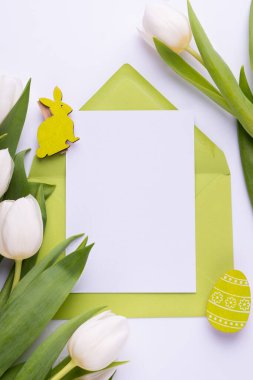 Template for Easter greeting card. Blank card with an envelope, a bouquet of white tulips and decorative eggs and a rabbit.