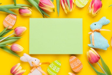 Template for Easter greeting card. Blank card with a bouquet of tulips and decorative eggs and a rabbit. Flat lay. Spring composition.