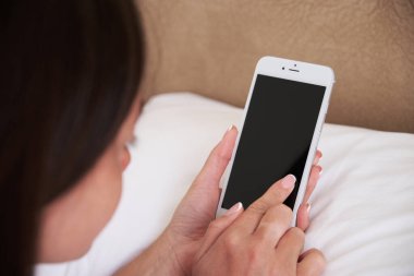 Genç kadın yatak odasında yatakta yatarken akıllı telefon kullanıyor. Yakın plan akıllı telefon ekranı. Mocap mobil uygulaması