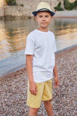 Saman şapkalı ve deniz kıyısında beyaz tişörtlü şık bir gencin portresi. Yaz tatili ve seyahat kavramı.