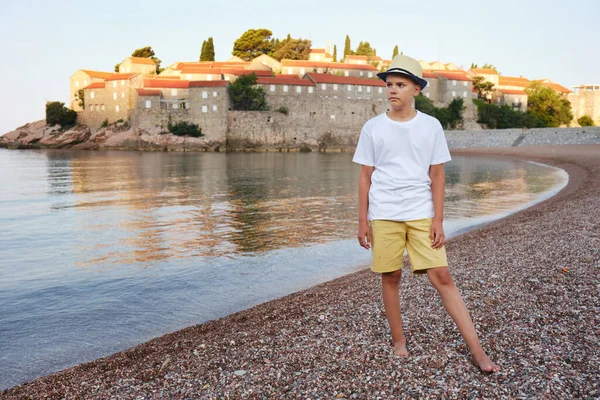 stock image Portrait of a stylish teenage boy in a straw hat and a white t-shirt on the seashore. The concept of summer vacation and travel.