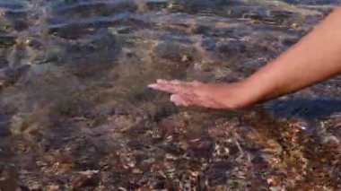 Genç kadınların elleri denizde suya dokunuyor. Deniz kıyısındaki tatil ve seyahat konsepti.