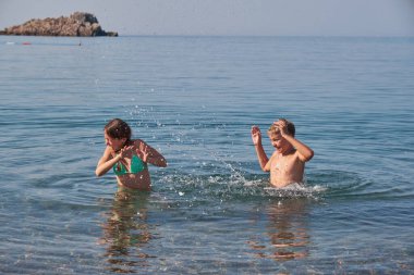 Neşeli oğlan ve kız denizde yüzer ve su sıçrar. Güneşli yaz günü, tatil günü