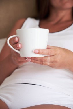 Beyaz bardak, sabah yatak odasındaki yatakta oturan genç bir kadının ellerinde. Tasarımın için bir model.