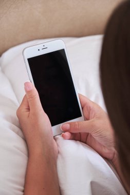 Genç kadın yatak odasında yatakta yatarken akıllı telefon kullanıyor. Yakın plan akıllı telefon ekranı. Mocap mobil uygulaması