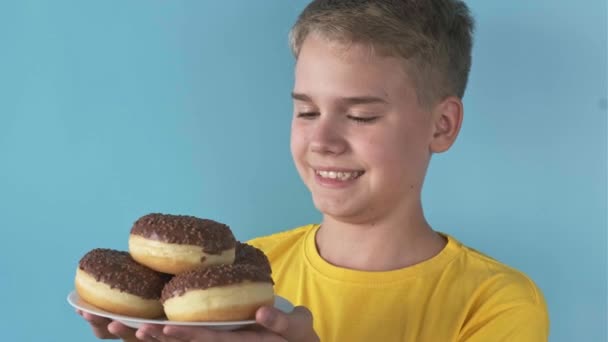 Щасливий Підліток Виглядає Передчуттям Повній Тарілці Шоколадних Пончиків Синьому Фоні — стокове відео