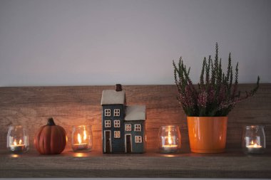 Oturma odasındaki bir rafta sonbahar kompozisyonu. Dekoratif ev, mumlar, fırın ve balkabağı. Hygge ev dekorasyonu için şirin bir sonbahar düzenlemesi.