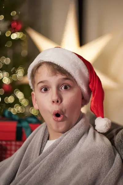 Funny portrait of a boy at Christmas. A teenager in a Santa hat near a Christmas tree.