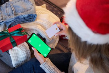 Bir kadın akıllı telefon ve kredi kartı kullanıyor. Başvuru ya da hizmet için bir model. Noel alışverişi ve indirimleri.