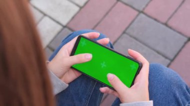 Krom anahtar yeşil ekranda, akıllı telefonun yakın plan görüntüsü. Genç kız dışarıda akıllı telefon kullanıyor, mesaj yazıyor ya da oynuyor..