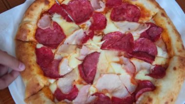 Eller pepperonili pizzanın porsiyonlarını alır. Masada pizza hazır. İnsanlar pizzacıda lezzetli pizza dilimleri alıyorlar. Üst Manzara. Salamlı ve peynirli taze pizza..