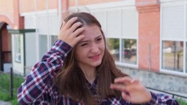 Ekose gömlekli genç bir kız rüzgarlı bir günde, açık havada, dağınık saçlardan rahatsız olur..