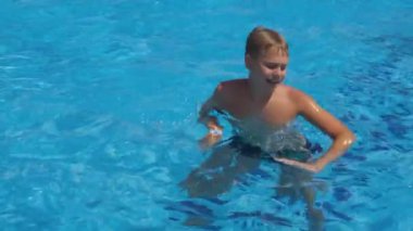 Çocuk yüzme havuzunun parlak mavi sularında mutlu bir şekilde dans ediyor..