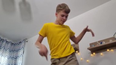 Genç çocuk evde enerjik bir şekilde dans ediyor, etkileyici hareketler sergiliyor ve müzikten zevk alıyor.