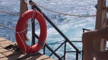 Deniz kıyısındaki ahşap iskele çitlerinde asılı turuncu bir can simidi, deniz güvenlik şamandırası.