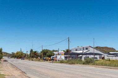 Petrusville, South Africa - Feb 21, 2023: A street scene, with a business, vehicles and street maintenance workers, in Petrusville in the Northern Cape Province