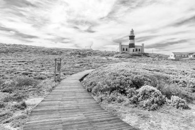 Afrika 'nın en güney ucundaki tarihi Agulhas deniz feneri, Cape Agulhas. Deniz fenerine giden tahta yol görünür. Tek Renkli