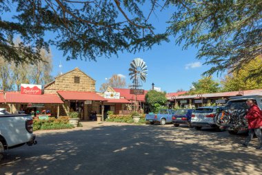 Clarens, Güney Afrika - 4 Mayıs 2025 Clarens 'de bir sokak sahnesi. İş yerleri, insanlar, bir yel değirmeni ve araçlar görünür.