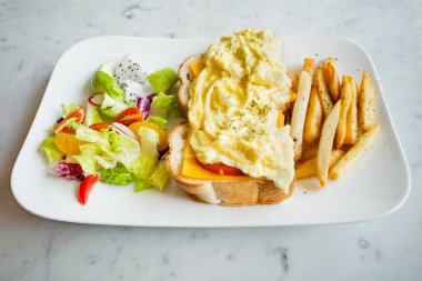 Peynirli omlet, beyaz ekmek, karışık sebzeler ve tabakta patates kızartması.