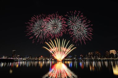 Gece gökyüzünde çeşitli renklerde renkli havai fişekler ve suda yansımalar.