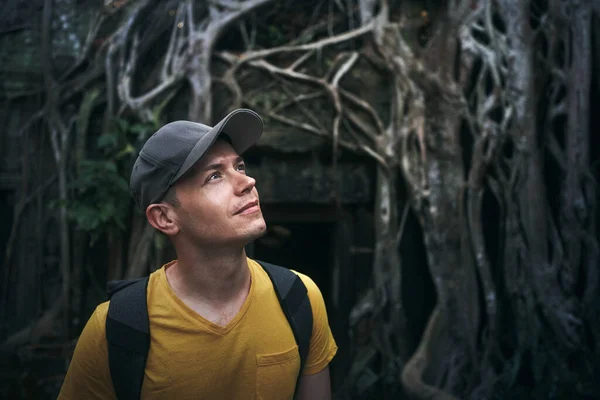 男は木の巨大な根の下で生い茂った古代の寺院を賞賛 カンボジアの観光客の肖像 — ストック写真