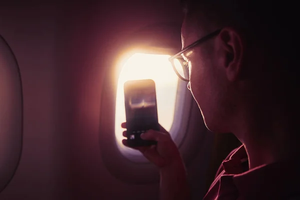 通过飞机窗户拍照时的人物形象 在美丽的落日下 乘客在飞行途中使用电话 — 图库照片