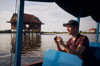 Gölde yüzen teknede kameralı turist portresi. Kamboçya 'da Siem Reap yakınlarında Tonle Sap Gölü' nde yüzen köy