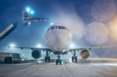 Uçuştan önce uçağın sulanması. Kar yağarken havaalanında kış gecesi