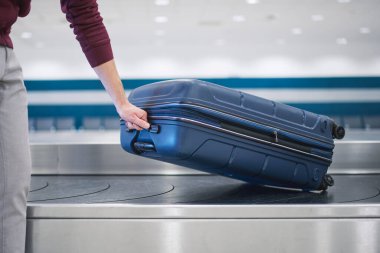 Traveling by airplane. Passenger pick up his blue suitcase in baggage claim in airport terminal.