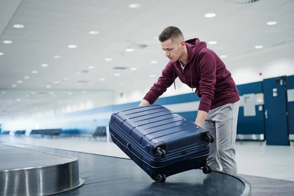 stock image Traveling by airplane. Passenger pick up his blue suitcase in baggage claim in airport terminal