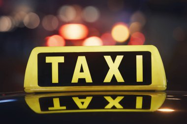 Selective focus on taxi sign on roof of car against busy city street at night.