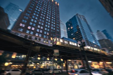 Chicago 'da demiryolu yükseltilmiş. Gece şehir merkezindeki gökdelenlere karşı bulanık hareketli toplu taşıma treni