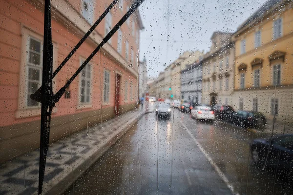Rain in city. Selective focus on raindrops on window of tram against traffic on a busy urban street in rainy day