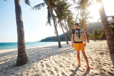 Sırt çantalı turistin palmiye ağaçlarıyla kumsalda yürüyüp gün batımını izlediği arka manzara. Cham Adaları, Vietnam