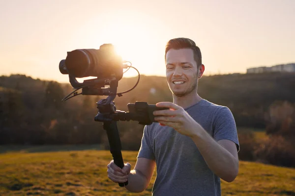 カメラとジンバルで撮影しながら笑顔の男 美しい夕日の風景に対する幸せなビデオカメラマンの肖像 — ストック写真